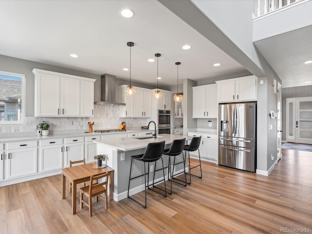 kitchen with wall chimney exhaust hood, light wood-type flooring, white cabinetry, and stainless steel appliances