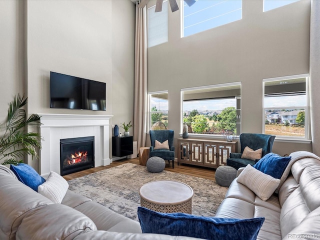 living room with a tiled fireplace, ceiling fan, wood-type flooring, and a high ceiling