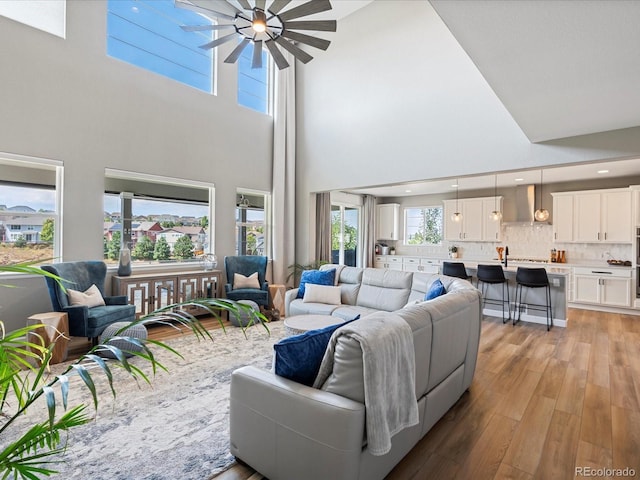 living room with ceiling fan, light wood-type flooring, and a high ceiling