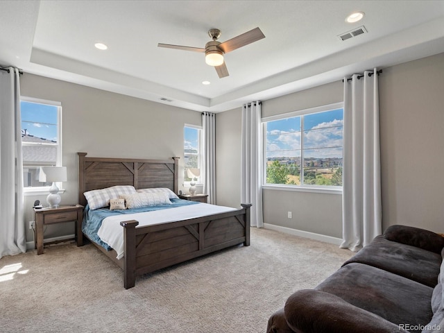 bedroom with light colored carpet, a raised ceiling, and ceiling fan