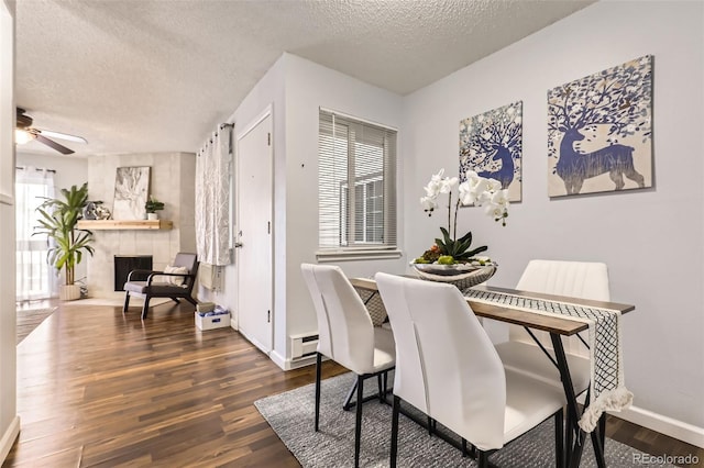 dining space with a textured ceiling, dark wood-type flooring, and a tile fireplace