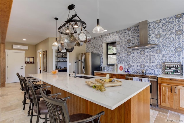 kitchen featuring stone tile floors, stainless steel appliances, a sink, wall chimney range hood, and light stone countertops