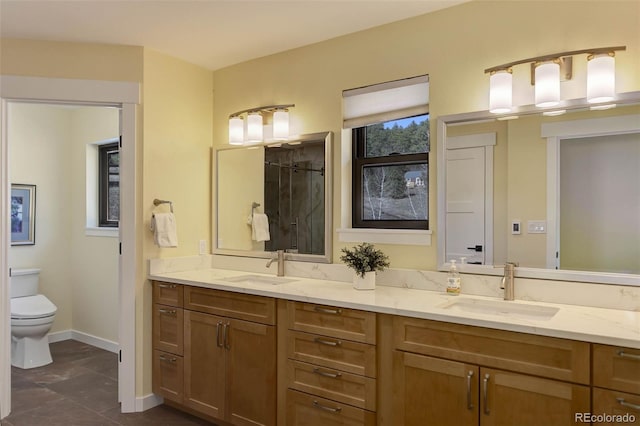 bathroom featuring baseboards, a sink, toilet, and double vanity