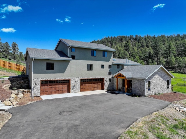 20101 Spring Gulch Rd, Morrison, CO 80465 - view of front of house featuring an attached garage, driveway, stone siding, stucco siding, and a view of trees