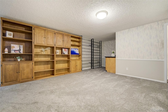 unfurnished living room featuring light carpet, a textured ceiling, and baseboards