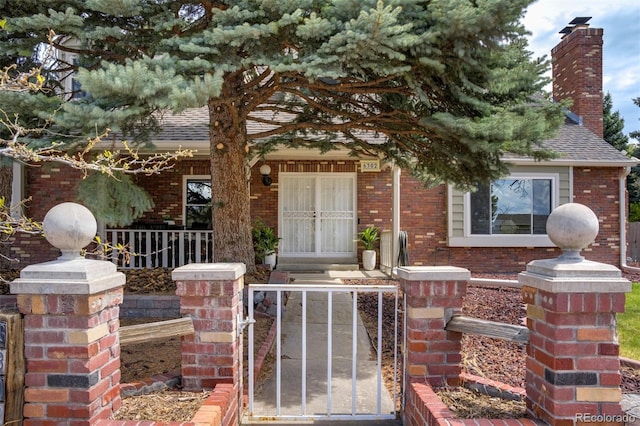 doorway to property with brick siding, fence, and a shingled roof