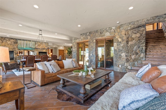 living room featuring beamed ceiling, wood-type flooring, and a stone fireplace