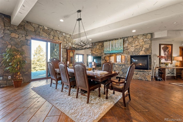 dining space featuring a stone fireplace, hardwood / wood-style floors, and beam ceiling