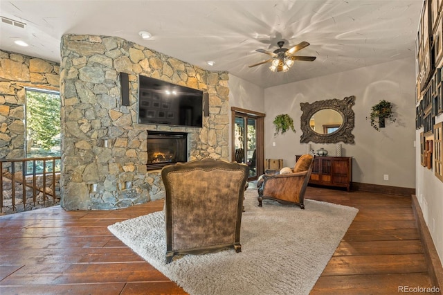 living room with ceiling fan, a stone fireplace, a healthy amount of sunlight, and dark hardwood / wood-style flooring