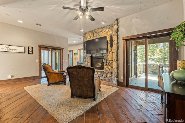 living room featuring hardwood / wood-style flooring, ceiling fan, and a stone fireplace