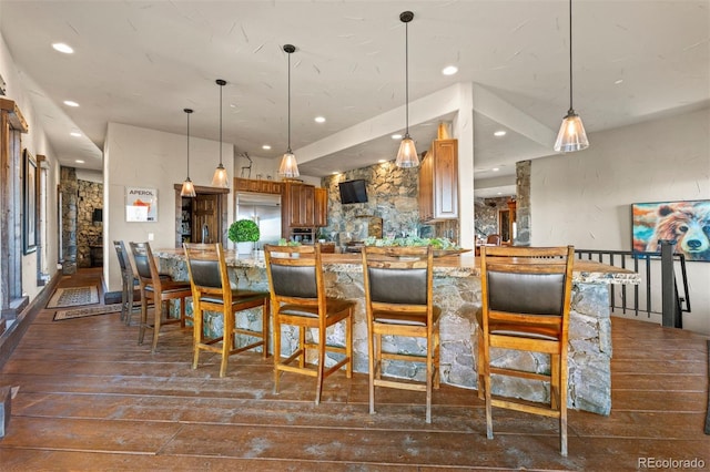 kitchen with pendant lighting, stainless steel built in refrigerator, dark hardwood / wood-style floors, and a breakfast bar