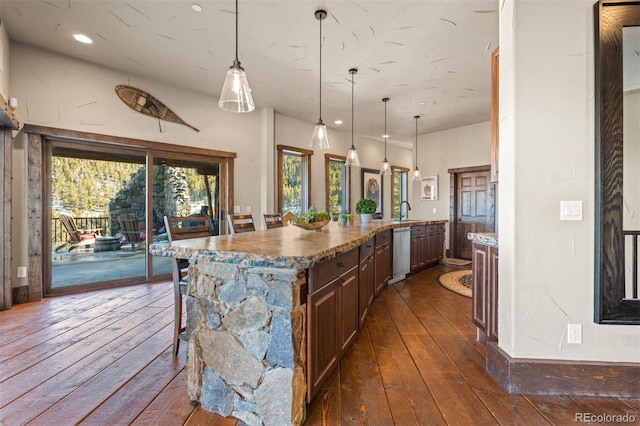 kitchen with dark hardwood / wood-style flooring, hanging light fixtures, stainless steel dishwasher, and a kitchen bar