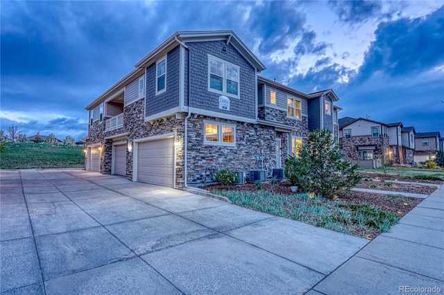 view of home's exterior with a garage, central air condition unit, driveway, and stone siding