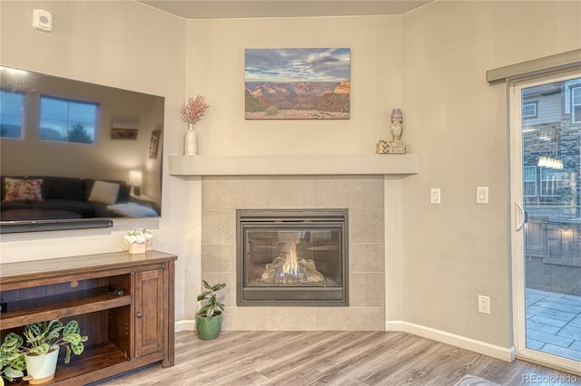 living area with baseboards, wood finished floors, and a tile fireplace