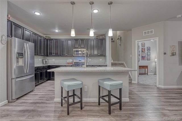kitchen with light wood-style floors, a breakfast bar area, a sink, appliances with stainless steel finishes, and backsplash