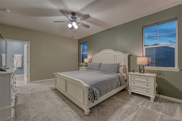 bedroom featuring baseboards, ceiling fan, ensuite bathroom, and light colored carpet