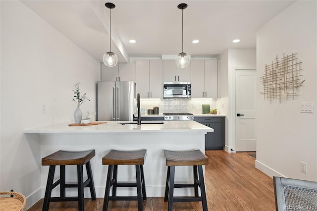 1238 N Tennyson St, Denver, CO 80204 - kitchen featuring a peninsula, a kitchen bar, light countertops, appliances with stainless steel finishes, and tasteful backsplash