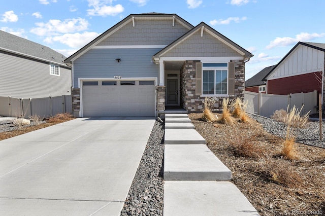 craftsman-style house with concrete driveway, an attached garage, fence, and stone siding