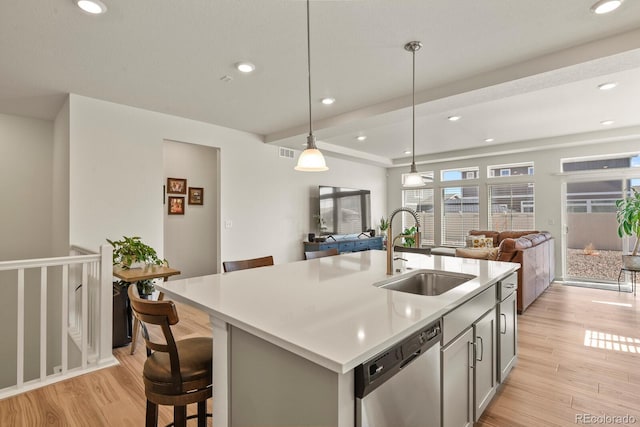 kitchen with stainless steel dishwasher, light countertops, light wood finished floors, and a sink