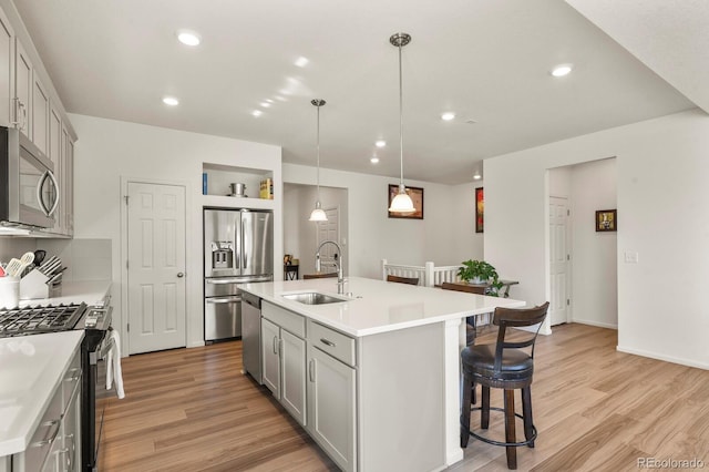 kitchen featuring light wood finished floors, a sink, light countertops, appliances with stainless steel finishes, and a kitchen bar