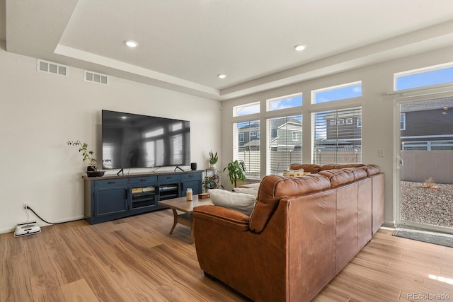 living room featuring visible vents, light wood-style flooring, and a raised ceiling