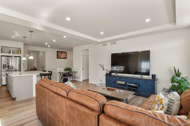 living area with a tray ceiling, recessed lighting, light wood-type flooring, and visible vents