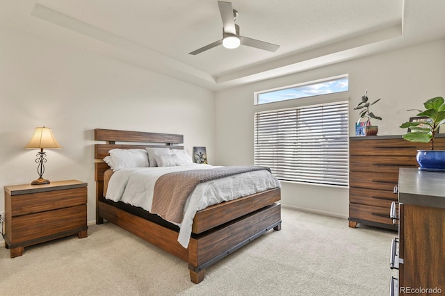 bedroom with a tray ceiling, light carpet, baseboards, and ceiling fan