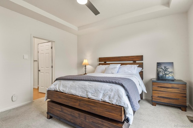 bedroom featuring a tray ceiling, light carpet, baseboards, and ceiling fan