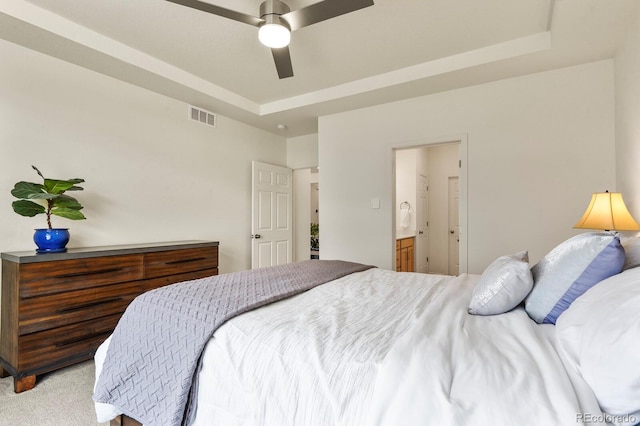 bedroom with visible vents, light colored carpet, ensuite bath, and a raised ceiling