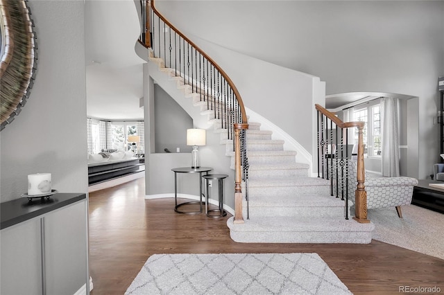 staircase with a wealth of natural light, a towering ceiling, and wood finished floors