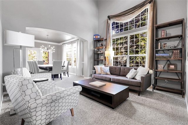 carpeted living room with ornamental molding, arched walkways, baseboards, and a notable chandelier
