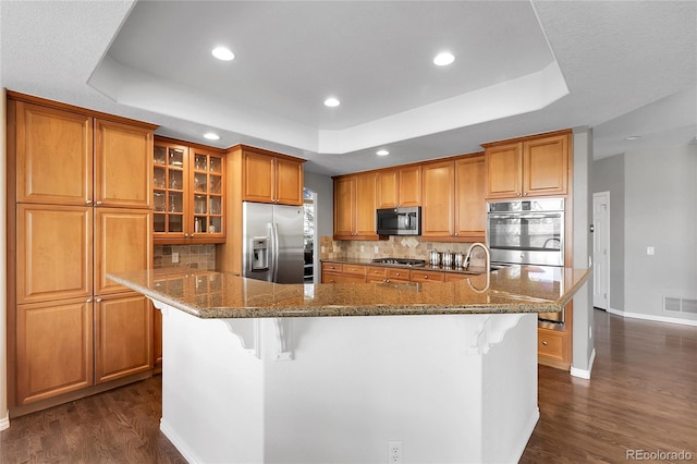 kitchen featuring dark wood finished floors, stainless steel appliances, brown cabinets, and a raised ceiling
