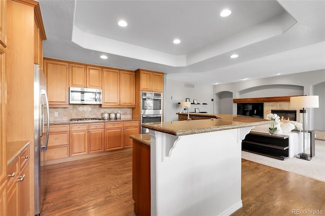 kitchen featuring light wood-style flooring, a tray ceiling, a breakfast bar area, a kitchen island with sink, and appliances with stainless steel finishes