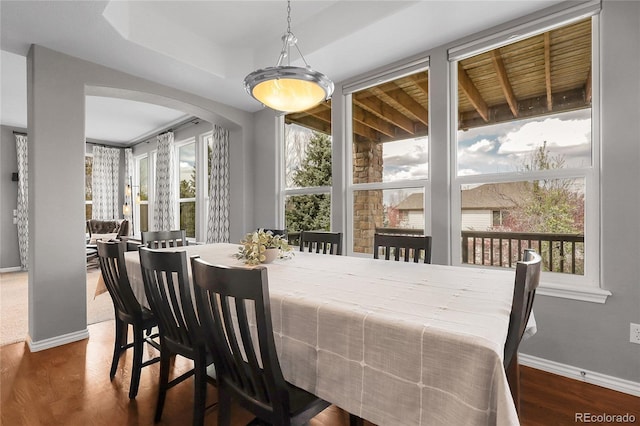 dining space featuring wood finished floors, baseboards, and arched walkways