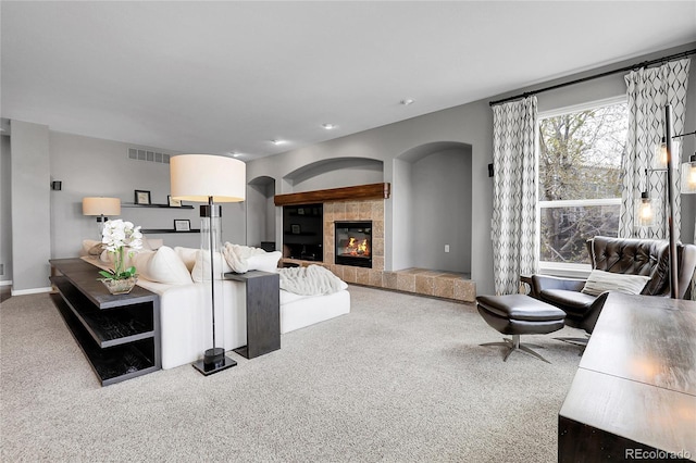 carpeted living room with arched walkways, a tile fireplace, visible vents, and baseboards