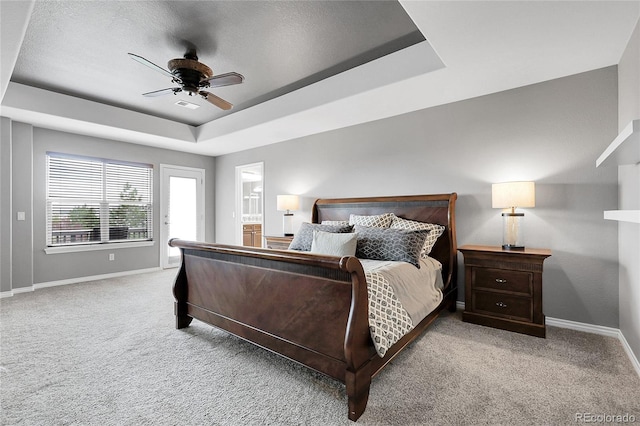 carpeted bedroom featuring a tray ceiling, baseboards, a ceiling fan, and visible vents