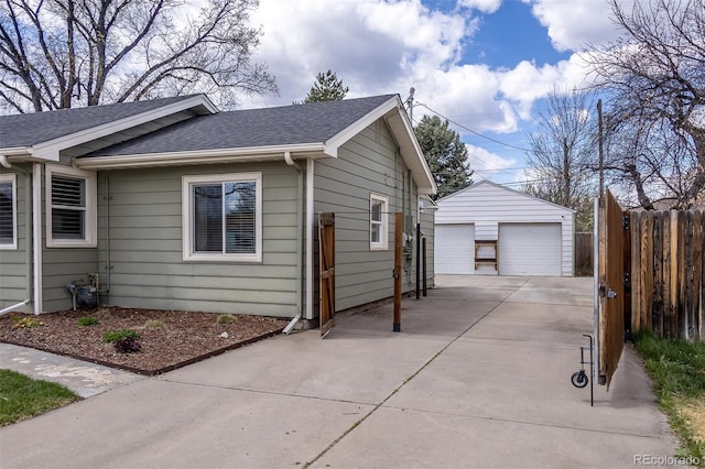 view of home's exterior featuring a detached garage, fence, an outbuilding, and roof with shingles