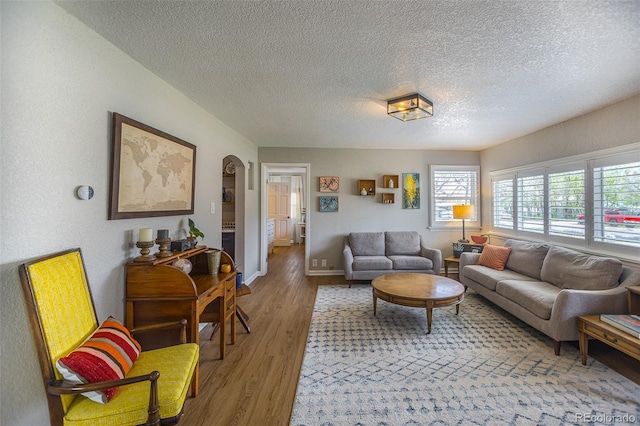 living area with light wood-style floors, arched walkways, baseboards, and a textured ceiling
