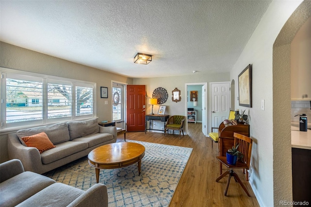 living area with arched walkways, a textured ceiling, and wood finished floors