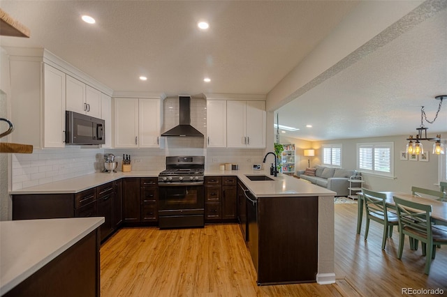 kitchen featuring a sink, light countertops, wall chimney exhaust hood, a peninsula, and black appliances