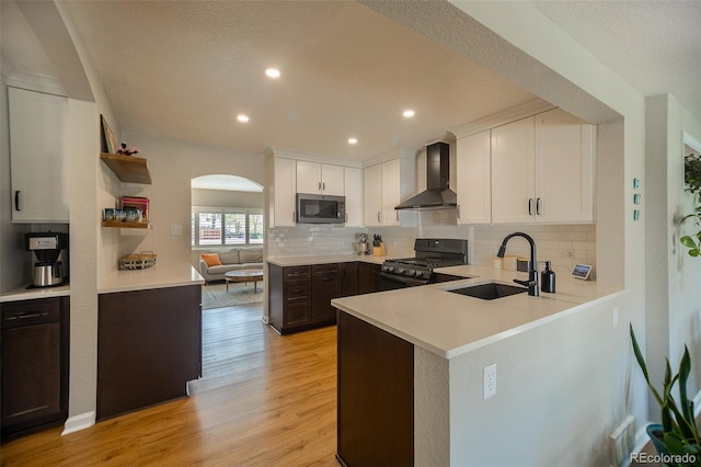 kitchen featuring arched walkways, tasteful backsplash, a sink, stainless steel appliances, and wall chimney exhaust hood