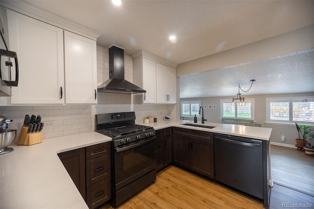 kitchen featuring black gas stove, dishwashing machine, wall chimney range hood, light countertops, and a sink