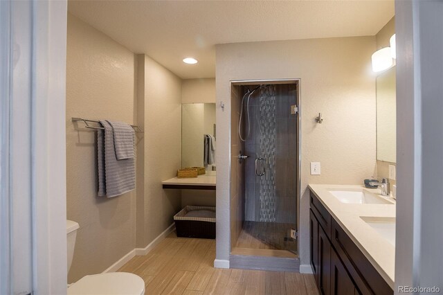 bathroom featuring a textured wall, wood finished floors, toilet, a shower stall, and a sink