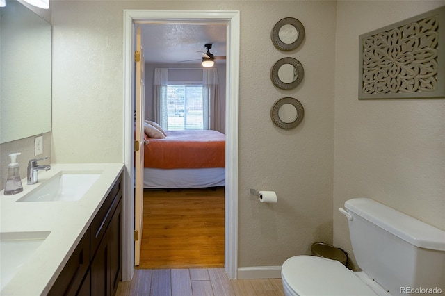 bathroom featuring a ceiling fan, wood finished floors, a sink, toilet, and ensuite bath