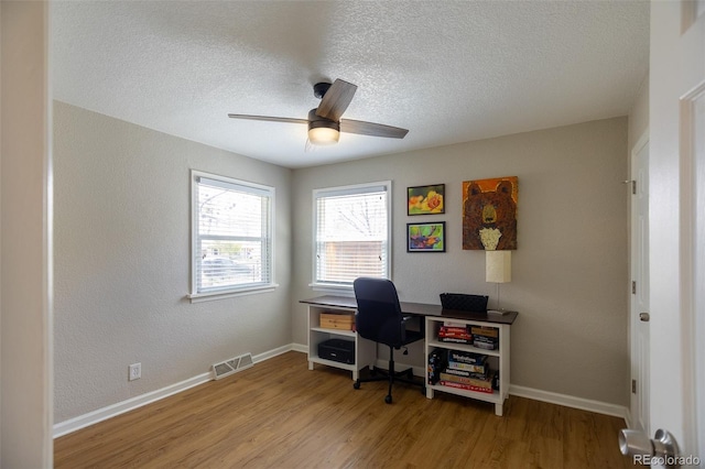 office with a textured ceiling, ceiling fan, wood finished floors, and visible vents