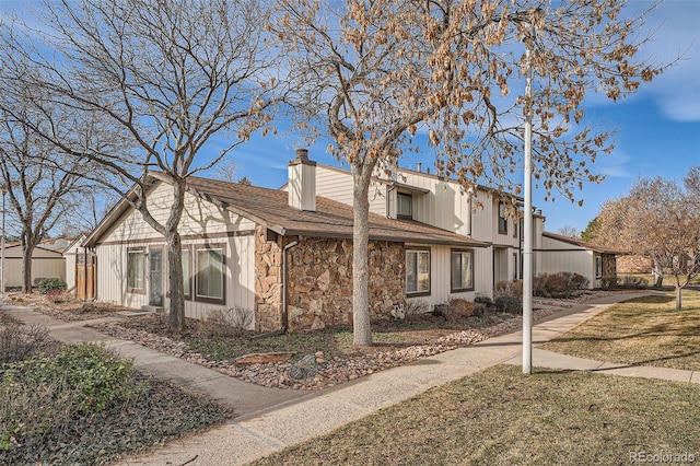 view of front of house featuring stone siding, a chimney, and roof with shingles