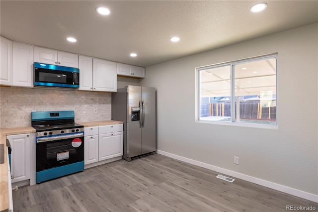 kitchen with stainless steel appliances, light wood-type flooring, white cabinets, and backsplash