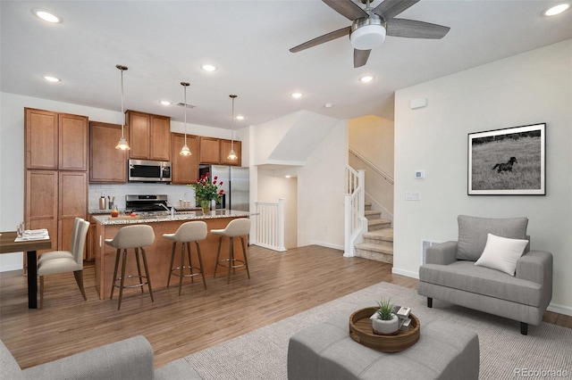 living area featuring a ceiling fan, light wood-type flooring, stairway, baseboards, and recessed lighting
