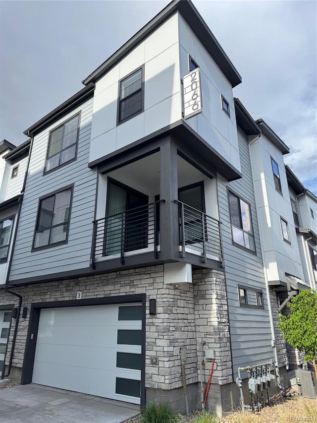 exterior space featuring driveway, an attached garage, stone siding, and a balcony