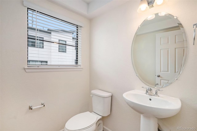 half bath with toilet, baseboards, and a sink